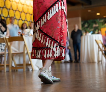 native american woman walking on a wooden floor dressed in a red dress